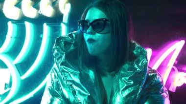 Geceleri parlayan neon duvarın yanında bin yıllık esrarengiz güzel kız. Gözlüklü gizemli hipster genç. Parlak lazer ceket ve güneş gözlüğü giyen güzel şık genç. kötü yaşam tarzı.