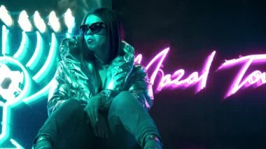 Geceleri parlayan neon duvarın yanında bin yıllık esrarengiz güzel kız. Gözlüklü gizemli hipster genç. Parlak lazer ceket ve güneş gözlüğü giyen güzel şık genç. kötü yaşam tarzı.