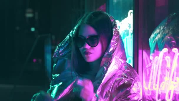 Millennial cool modern pretty girl smoking cigarette near glowing neon wall at night. Mysterious hipster. Beautiful stylish teen wearing shiny laser jacket and sunglasses. bad lifestyle. — Stock Video