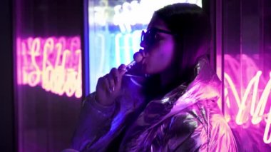 Kürk gözlük genç moda genç kız sokak neon mavi pembe işareti ile aydınlatılmış bir şeker yalıyor, trendy gece ışık güzel bin yıllık kadın 80'lerin kavramı geri kızdırma. Ağızda büyük lolipop.