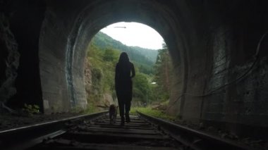 Tüneldeki bir kızın silueti. Köpeği olan bir kız raydan çıkar. Tünelden çıkıyor.