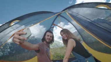 Çadırda bulunan mutlu çift gezginler akıllı telefonda selfie çekiyor. Sosyal ağlar için bir fotoğraf çekin. Sarı çadır. Dağlarda yürüyüş