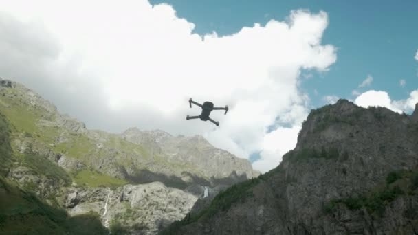 Drone met draaiende propellers die in de lucht hangen op een achtergrond van meer en bergen. Drone met een camera zweeft in de lucht. Close-up van een vliegtuig en mesjes die draaien — Stockvideo