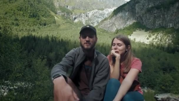 山の中の旅行者の男女の幸せなカップルは、スマートフォンで自分撮りを取ります。ソーシャルネットワークのために写真を撮ります。山でのハイキング — ストック動画