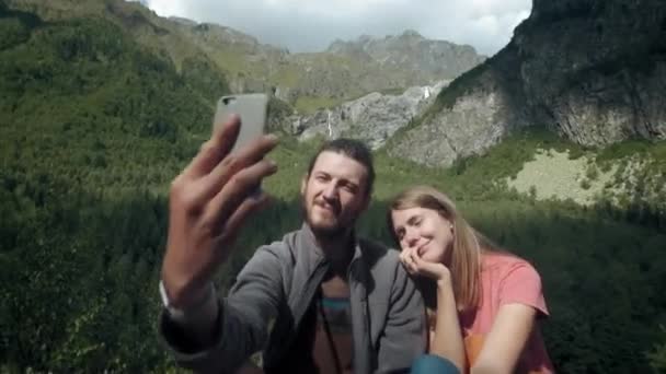 Happy couple of travelers man and woman in the mountains take selfie on smartphone. Take a photo for social networks. Hiking in the mountains — Stock Video