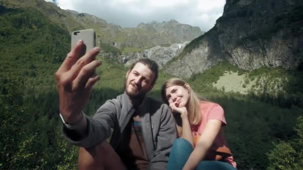 Happy couple of travelers man and woman in the mountains take selfie on smartphone. Take a photo for social networks. Hiking in the mountains — Stock Video