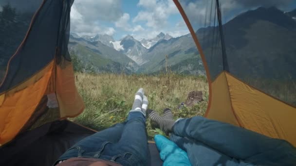 Vue de l'intérieur d'une tente sur les montagnes. Deux voyageurs, hommes et femmes, sont couchés dans une tente. Prenez une pause du sentier de randonnée le long de la route de montagne. Pieds sortis de la tente . — Video