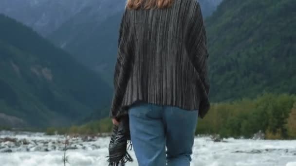 Giovane ragazza attraente viaggiatore-blogger Alza le mani, gioisce alla vista delle montagne. Vestita con abiti caldi e un plaid. Camminando lungo un fiume di montagna. Svaneti, Georgia — Video Stock