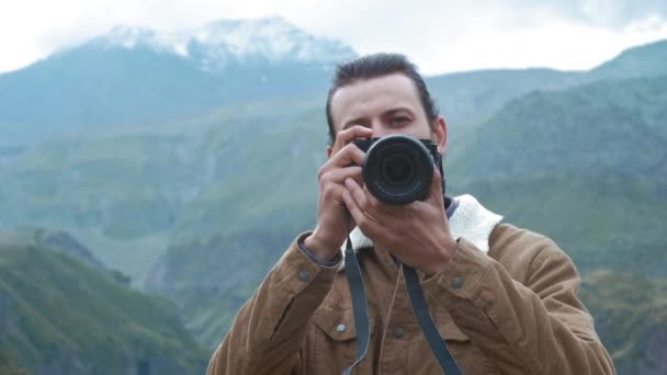 PORTTAIT: Fotógrafo viajante masculino faz fotos de montanhas profissionais para blog. Um tipo com cabelo comprido e barba a segurar uma câmara profissional nas mãos. Expedição às montanhas . — Vídeo de Stock