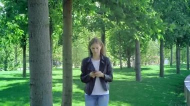 Kafası karışmış bir kadının akıllı telefon içeriğini kontrol eden bir kadının ön görünümü ve ardından parktaki kameraya bakmayı bırakması. Sokak kıyafetleri giyen genç bir kız sürpriz bir şekilde akıllı telefonuna bakıyor. Şok edici ileti