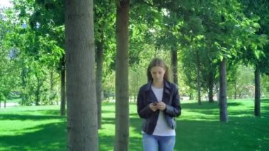 Kafası karışmış bir kadının akıllı telefon içeriğini kontrol eden bir kadının ön görünümü ve ardından parktaki kameraya bakmayı bırakması. Sokak kıyafetleri giyen genç bir kız sürpriz bir şekilde akıllı telefonuna bakıyor. Şok edici ileti