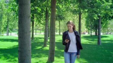 Genç güzel kız bir akıllı telefon ile parkta yürüyor. Mesajı okur ve çok mutlu. Dans ve mutluluk ve sevinç ile sıçrayan.