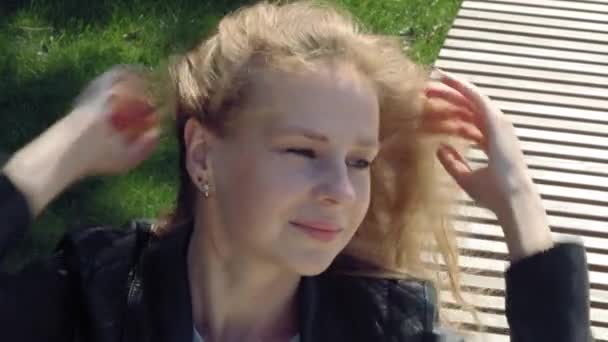 Zbliżenie: Młoda piękna dziewczyna w ulicznych ubraniach w parku rozpuszcza długie brązowe włosy na wietrze. Gra z fryzurą podczas wietrznej pogody jesienią lub latem — Wideo stockowe