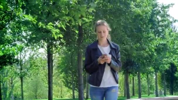 젊은 아름다운 소녀는 스마트 폰으로 공원에서 걷고있다. 메시지를 읽고 매우 행복합니다. 행복과 기쁨으로 춤추고 튀는. — 비디오