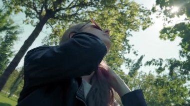 Parktaki kameraya poz veren uzun saçlı güzel genç kız modeli, yeşil ağaçların arka planında. Bir selfie için iyi bir poz arar. Deri ceket giymiş