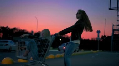 Yavaş hareket iki genç milenyum kız birlikte alışveriş arabaları ve geceleri süpermarket park kıvılcım üzerinde yarış eğleniyoruz. Alışveriş arabasına binmek, özgürlüğün ve gençliğin tadını çıkarmak.