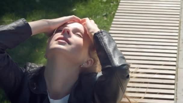 Nahaufnahme: junges hübsches Mädchen in Straßenkleidung im Park löst lange braune Haare im Wind auf. spielt mit einem Haarschnitt bei windigem Wetter im Herbst oder Sommer — Stockvideo