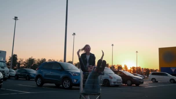 Cámara lenta dos jóvenes millennials chica se divierten juntos carreras en carritos de compras y bengalas en el estacionamiento del supermercado por la noche. Montar en un carrito de compras, disfrutar de la libertad y la juventud . — Vídeo de stock