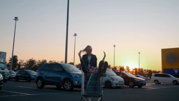 Ralentissez deux jeunes filles milléniales s'amusent ensemble en course sur des chariots et des étincelles au parking du supermarché la nuit. Monter dans un panier, profiter de la liberté et de la jeunesse . — Video