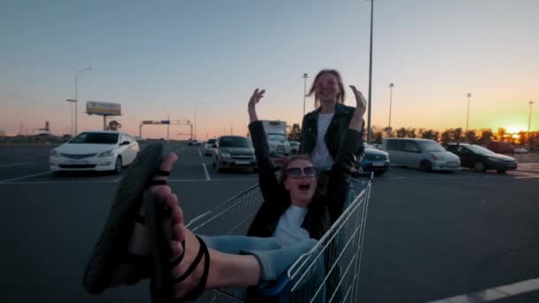 Al rallentatore due giovani millennials girl si stanno divertendo insieme correndo su carrelli della spesa e scintillanti al parcheggio del supermercato di notte. Cavalcando un carrello della spesa, godendo della libertà e della gioventù . — Video Stock