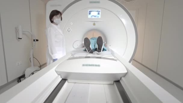 Az orvos MRI vizsgálatot végez egy betegnél a klinikán. A lány az MRI-ben fekszik. Mágneses rezonanciás képalkotás az emberi test tanulmányozásában. Modern technológiák az orvostudományban — Stock videók