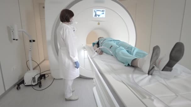 De dokter doet een MRI scan voor een patiënt in de kliniek. Het meisje ligt in het MRI apparaat. Magnetische resonantie beeldvorming in de studie van het menselijk lichaam. Moderne technologieën in de geneeskunde — Stockvideo