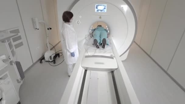 Az orvos MRI vizsgálatot végez egy betegnél a klinikán. A lány az MRI-ben fekszik. Mágneses rezonanciás képalkotás az emberi test tanulmányozásában. Modern technológiák az orvostudományban — Stock videók