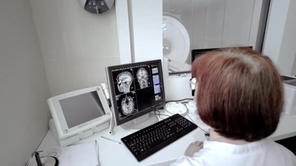 医者の技術者がMRIスキャンを監視してる。人間の体の研究で磁気共鳴画像。専門家は研究室のモニターを見ている — ストック動画