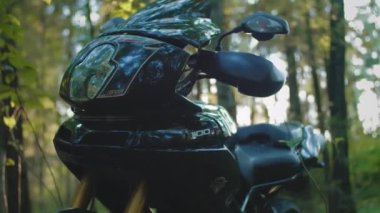 Motosikletli bir bisikletçi motosiklet koltuğunda oturur. Çalıştırır ya da çalıştırır. Bisiklet gezisine hazırlanıyorum. Ormanda gün batımında