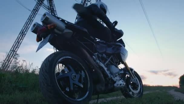 Motorrijder biker zit op een motorfiets. Start een fiets, rijdt de zonsondergang tegemoet langs een landweg. Alleen reizen. Avonturen op een kattenfiets in de natuur. Een romantische man. — Stockvideo