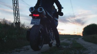 Motosikletli bir motorcu motosiklete biner. Bisikleti çalıştırıyor, gün batımına doğru gidiyor bir kır yolu boyunca. Yalnız seyahat et. Doğada kedi bisikleti maceraları. Romantik bir adam.