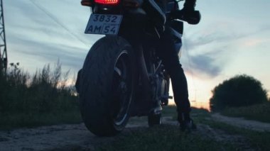 Motosikletli bir motorcu motosiklete biner. Bisikleti çalıştırıyor, gün batımına doğru gidiyor bir kır yolu boyunca. Yalnız seyahat et. Doğada kedi bisikleti maceraları. Romantik bir adam.
