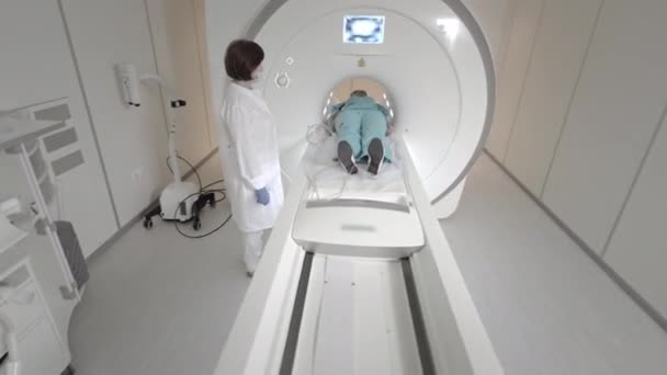 El médico hace una resonancia magnética para un paciente en una clínica. La chica yace en el dispositivo de resonancia magnética. Imágenes por resonancia magnética en el estudio del cuerpo humano. Tecnologías modernas en medicina. Examina los pulmones. — Vídeo de stock