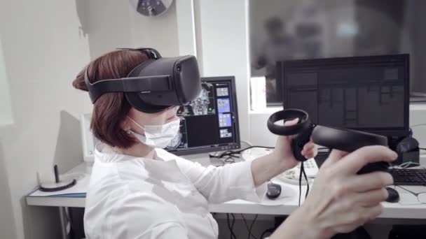 Concepto futurista: En el laboratorio médico, el cirujano que usa auriculares de realidad virtual utiliza controladores para operar de forma remota al paciente con robot médico. Avances de alta tecnología en medicina. — Vídeo de stock