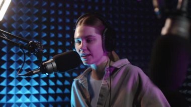 Güzel genç kız DJ mikrofona konuşuyor, podcast 'i kaydediyor ya da radyo için sabah haberlerini sunuyor. Podcast sunucusunun ya da DJ 'in mikrofondaki konuşmasını kapat. Profesyonel kulaklık takıyor..