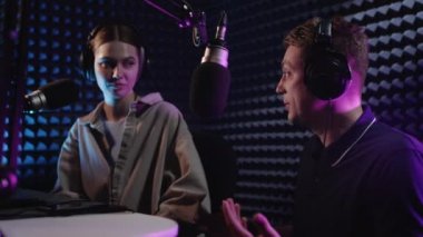 Podcast. İki yakışıklı genç adam müzik hakkında bir podcast sunuyor. Güzel bir kız ve bir adam profesyonel bir stüdyoda çalışıyor. Kız bir erkekle röportaj yapıyor. Bir yayın stüdyosunda mikrofona konuşmak.