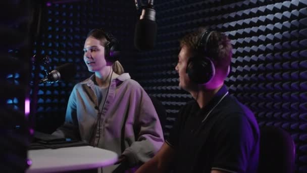 Professional radio recording studio. Beautiful DJ girl and young guy producer are recording a podcast. They create a radio broadcast. Dialogue together, discussing hot news. — Stock Video