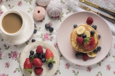 Çilek, ahududu, yaban mersini, muz ve pembe bir plaka üzerinde şurubu ile krep. Yatay. Üstten Görünüm