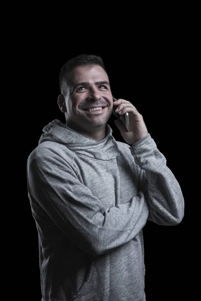 Portrait studio d'un homme souriant parlant sur un téléphone portable levant les yeux. Fond noir. Vertical . — Photo