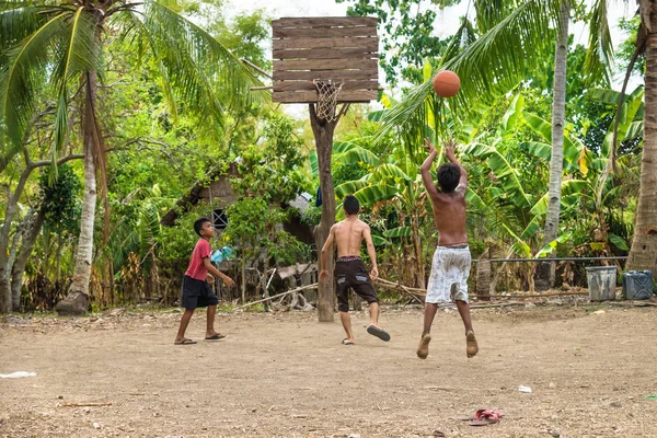 Sandugan, Siquijor, Filipinler - 13 Mayıs 2013: eski ahşap basketbol sepeti ile kum Field'da atlama bir basketbol oynayan üç çocuklar çocuk