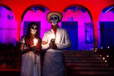 Merida, Cementerio genel, Meksika - 31 Ekim 2018: yakın customed erkek ve kadın ile Meksika geleneksel beyaz giysiler ve dia de los muertos Fest, için Event'de kemerli kırmızı pembe dökülen binanın önünde kafatası makyaj ile