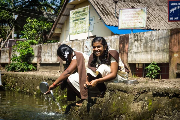 Chicas estudiantes lavando sus cuencos a lo largo del río en Kerala canal de remanso, Alleppey - Alappuzha, India Imagen De Stock