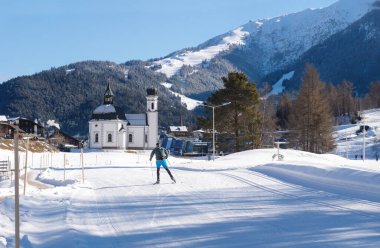 Avusturya 'nın tipik pitoresk kilisesi Seefeld, Avusturya' ya doğru güneşli pistte kros kayakçısı