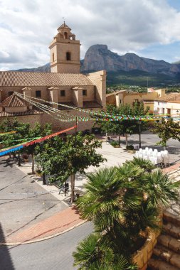 Polop de Marina Kilisesi 'nin renkli bayraklı ana meydanı kayalık sıradağlarla kaplı, Costa Blanca, İspanya