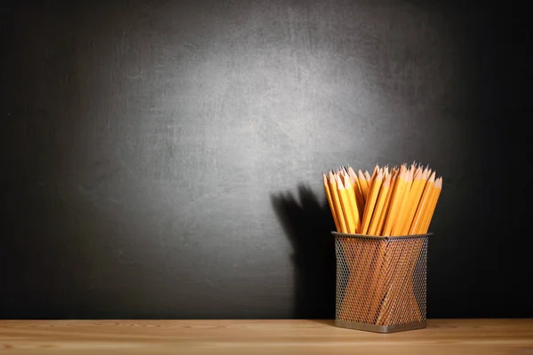 Pencils on a wooden school desk in front of a black chalkboard school. Education concept - the desk in the auditorium