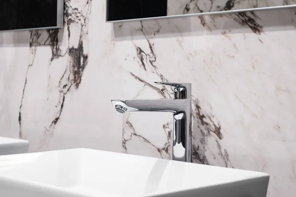 Luxury faucet mixer on white rectangular sink in interior of beautiful marble gray bathroom.