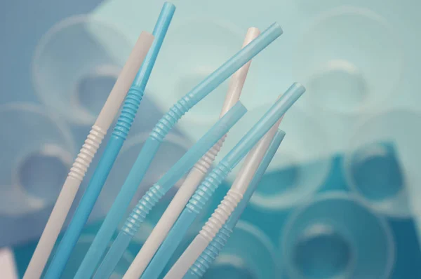 Açık arka planda plastik bardak önünde mavi ve beyaz plastik borular. Günlük yaşamda polimerler.