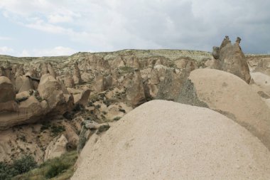 Türkiye 'nin Kapadokya kentindeki kayalık arazi. Dağlar yeşil ağaçlarla çevrili. Büyük taşlar.