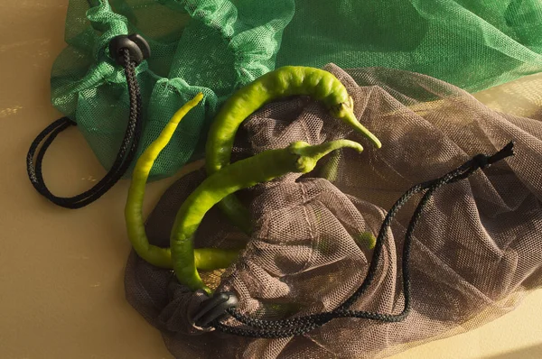 Yeşil biberlerin kahverengi, yeşil torbaların pastel sarısı arka planda yaratıcı düzeni. Plastik kirliliği azaltmak için çevre dostu çantalar.