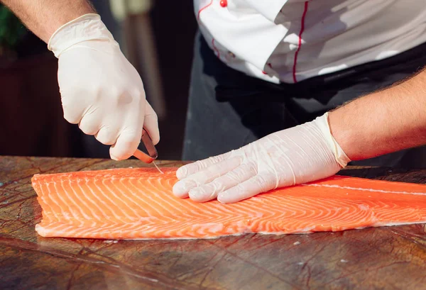 hands of chef cutting raw salmon fillet on table